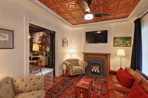 Living area featuring a fireplace, ceiling fan, an ornate ceiling, and wood finished floors