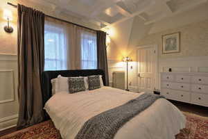 Bedroom featuring radiator heating unit, a wainscoted wall, beam ceiling, and coffered ceiling