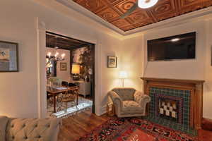 Living room with an ornate ceiling, a fireplace, wood finished floors, and ceiling fan with notable chandelier