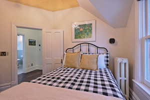 Bedroom with radiator, baseboards, dark wood-style floors, and vaulted ceiling