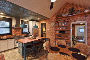 Kitchen featuring high end stainless steel range, wall chimney exhaust hood, wooden counters, lofted ceiling, and brick wall