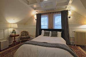 Bedroom featuring a decorative wall, radiator heating unit, wainscoting, coffered ceiling, and wallpapered walls