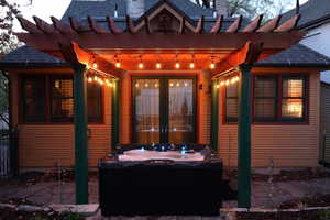 Rear view of property featuring a pergola, a patio area, french doors, and a hot tub