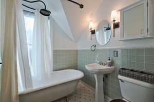 Bathroom featuring tile walls, toilet, a freestanding soaking tub, a wainscoted wall, and tile patterned flooring