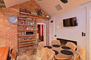 Dining room featuring wooden ceiling, brick wall, and lofted ceiling.