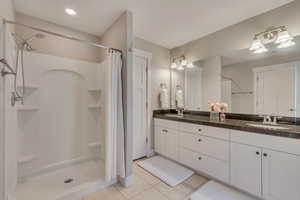 Full bath featuring a sink, a shower stall, tile patterned flooring, and double vanity
