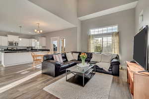 Living room with baseboards, a chandelier, recessed lighting, a towering ceiling, and light wood-style flooring