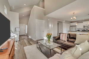 Living area featuring high vaulted ceiling, recessed lighting, light wood finished floors, baseboards, and a notable chandelier