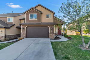 View of front of property featuring a front yard, an attached garage, stone siding, and concrete driveway