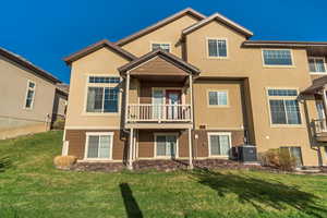 Back of property with cooling unit, a lawn, and stucco siding