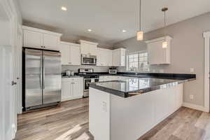 Kitchen featuring a peninsula, white cabinets, dark countertops, stainless steel appliances, and light wood finished floors