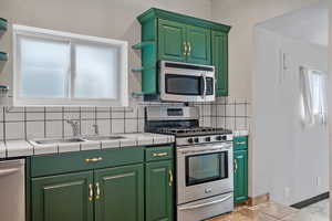 Kitchen with a sink, tile counters, decorative backsplash, and appliances with stainless steel finishes