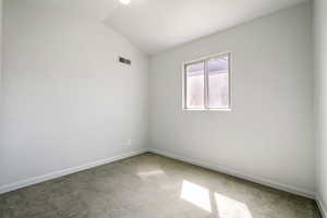 Carpeted spare room with visible vents, baseboards, and lofted ceiling