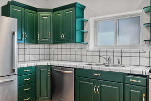 Kitchen with appliances with stainless steel finishes, tile counters, open shelves, decorative backsplash, and a sink