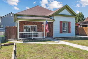 Bungalow-style home featuring stone siding, fence, a front lawn, and covered porch