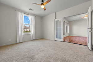 Carpeted empty room with french doors, visible vents, ceiling fan, and baseboards