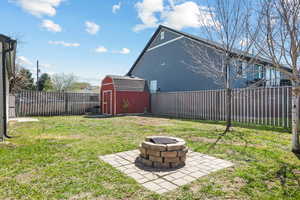 View of yard with a fenced backyard, an outdoor fire pit, an outdoor structure, and a storage unit