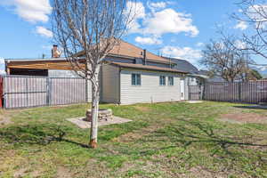 Back of property featuring fence, a fire pit, a gate, and a lawn