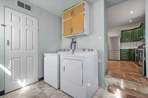 Washroom featuring visible vents, independent washer and dryer, and cabinet space
