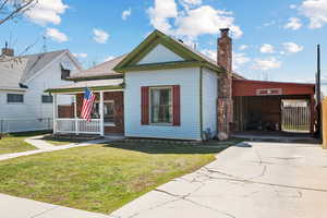 Bungalow-style home with a front yard, a porch, driveway, and a chimney