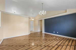 Unfurnished room featuring baseboards, high vaulted ceiling, a notable chandelier, and wood finished floors