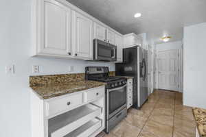 Kitchen with dark stone counters, baseboards, white cabinets, and stainless steel appliances