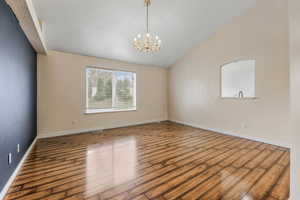 Empty room with baseboards, a notable chandelier, wood finished floors, and lofted ceiling