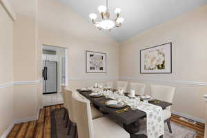 Dining room with baseboards, vaulted ceiling, an inviting chandelier, visible vents, and wood finished floors