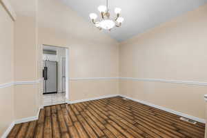 Empty room featuring baseboards, wood finished floors, a notable chandelier, and vaulted ceiling