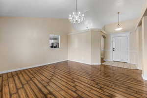 Foyer featuring arched walkways, wood finished floors, an inviting chandelier, and baseboards