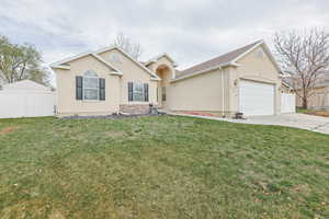 Single story home featuring an attached garage, concrete driveway, fence, and a front lawn