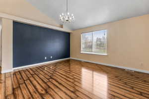 Empty room featuring wood finished floors, baseboards, an inviting chandelier, and lofted ceiling