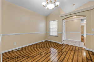 Unfurnished room featuring a notable chandelier, baseboards, visible vents, arched walkways, and wood finished floors