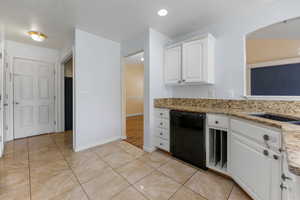 Kitchen with light tile patterned floors, white cabinets, light stone counters, dishwasher, and baseboards