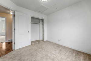 Unfurnished bedroom with visible vents, baseboards, a closet, carpet floors, and attic access