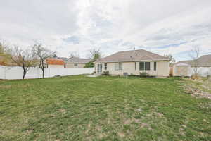 Back of property with stucco siding, an outdoor structure, fence, a lawn, and a storage unit