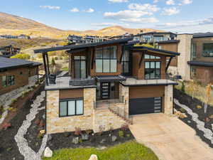 Contemporary house featuring stone siding, concrete driveway, a mountain view, a garage, and a balcony