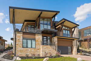 Contemporary house with stone siding, a balcony, a garage, and concrete driveway