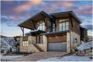 View of front facade with a balcony, stone siding, an attached garage, and driveway