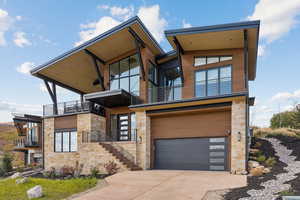 Contemporary home with a balcony, stone siding, concrete driveway, and stairs