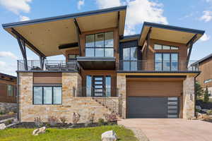 Modern home featuring stone siding, stairs, concrete driveway, an attached garage, and a balcony