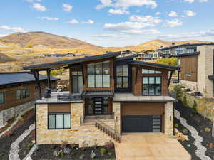 Contemporary house with driveway, stone siding, a mountain view, and an attached garage