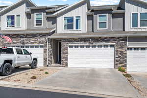 Multi unit property with board and batten siding, an attached garage, stone siding, and driveway