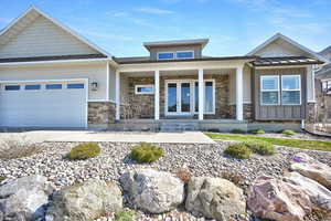 Craftsman-style home with an attached garage, a porch, stone siding, french doors, and driveway
