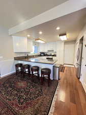 Kitchen with a kitchen breakfast bar, a peninsula, under cabinet range hood, stainless steel appliances, and hardwood / wood-style flooring