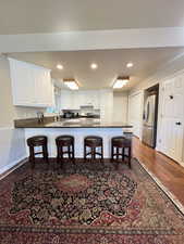 Kitchen featuring a breakfast bar, a peninsula, white cabinetry, dark countertops, and stainless steel appliances