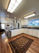 Kitchen with white dishwasher, a sink, open floor plan, a peninsula, and white cabinetry