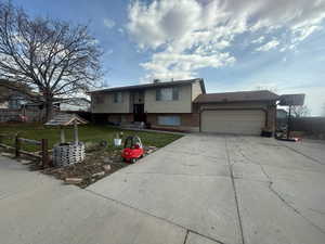 Bi-level home featuring concrete driveway, a front yard, brick siding, and an attached garage
