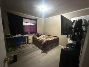 Bedroom with light wood-type flooring, a textured ceiling, and ornamental molding