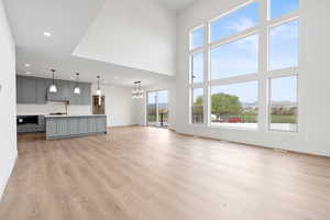 Unfurnished living room featuring a towering ceiling, a notable chandelier, baseboards, recessed lighting, and light wood-style floors